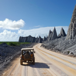 **Prompt 1: The Scarred Landscape and Adventurous Journey**
    "A surreal, rugged landscape of Nauru, showcasing the aftermath of extensive phosphate mining with sharp limestone pinnacles resembling a moonscape, under a vast tropical sky. A narrow, somewhat bumpy road winds through this unique terrain, with a small, sturdy vehicle driving along, conveying a sense of adventurous isolation and profound discovery. The atmosphere should be stark yet beautiful, emphasizing the island's unique geological features and the challenging journey to explore them."