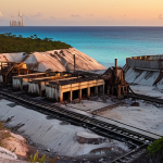 **A surreal landscape of Nauru's former phosphate mines at sunset.** Capture the stark, moon-like terrain with abandoned machinery, tinged with the warm colors of the setting sun. Focus on the contrast between the industrial past and the natural beauty of the island, emphasizing the environmental impact of mining. Include a hint of the ocean in the background.